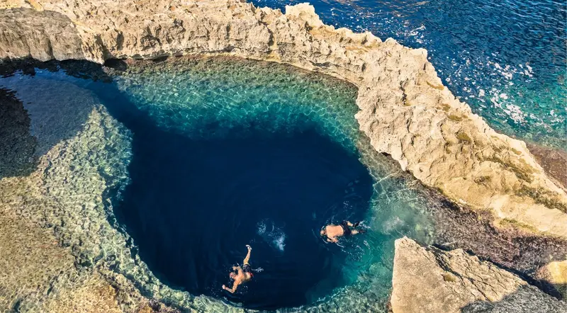 Swimmers snorkelling in a deep natural pool ringed by rock near Comino