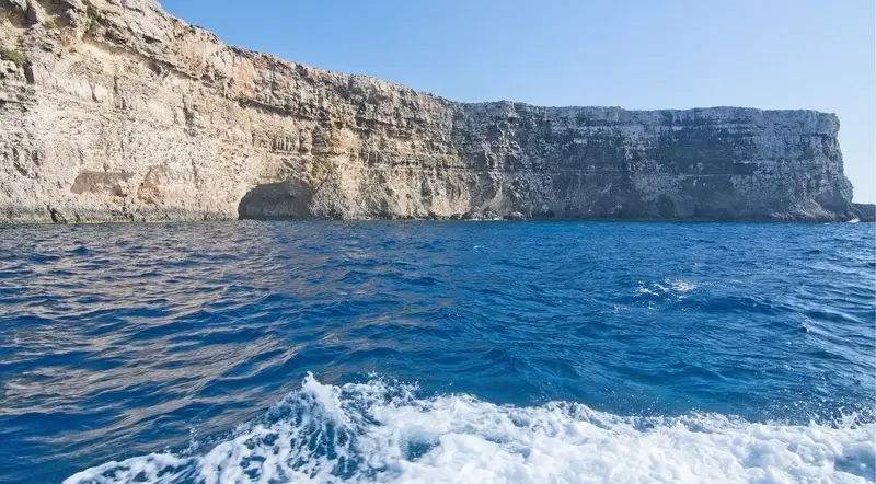 Comino's limestone cliffs seen from a cruise boat's wake on the open sea