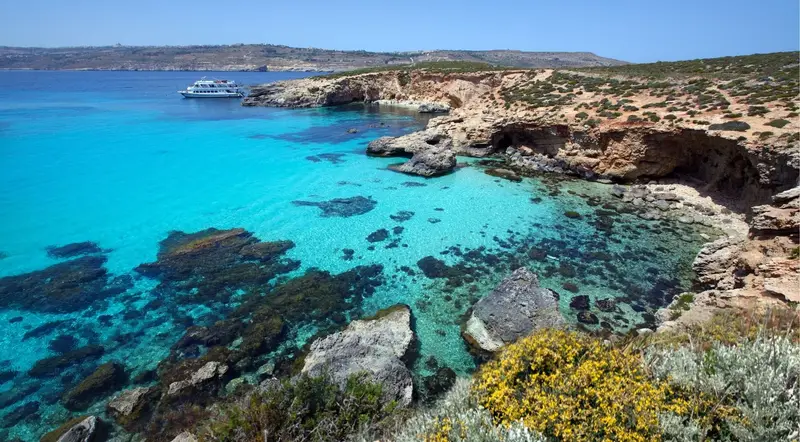 Crystal Lagoon cove on Comino with a boat moored in deep turquoise water below the cliffs