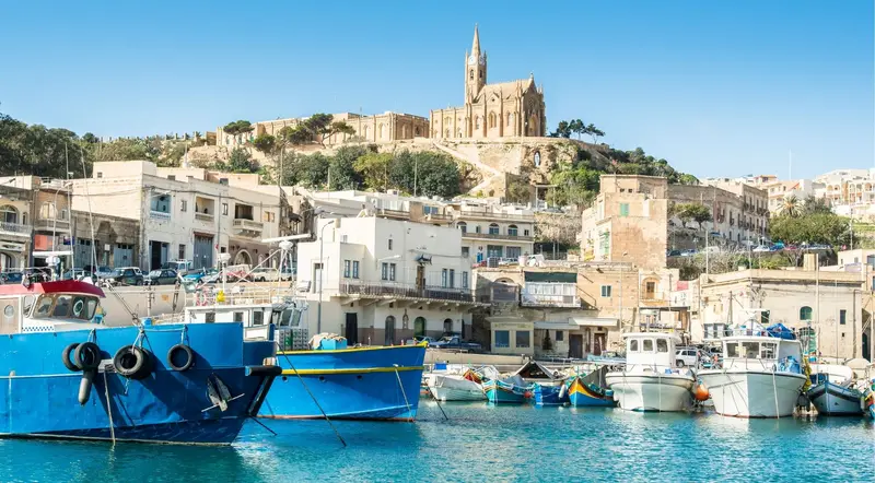 Mġarr Harbour on Gozo with fishing boats below the hilltop church