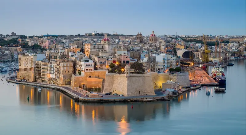 Malta's harbour bastions lit at dusk, the golden-hour light typical of a Blue Lagoon sunset cruise